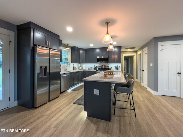 kitchen with light hardwood / wood-style floors, sink, appliances with stainless steel finishes, decorative light fixtures, and a center island