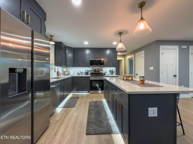 kitchen with light hardwood / wood-style floors, pendant lighting, appliances with stainless steel finishes, and a center island