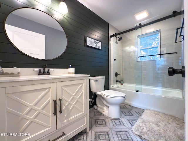 full bathroom featuring shower / bath combination with glass door, wood walls, toilet, and vanity