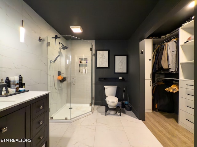 bathroom with tile walls, wood-type flooring, vanity, toilet, and a shower with shower door