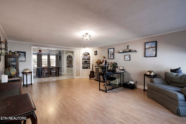 living room with built in shelves, light hardwood / wood-style floors, ornamental molding, and a textured ceiling