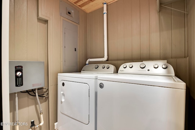 washroom with electric panel, wood walls, and washer and clothes dryer