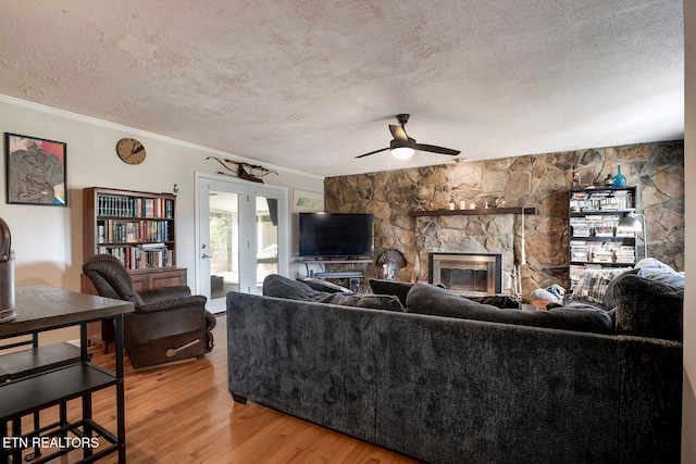 living room with crown molding, a stone fireplace, a textured ceiling, hardwood / wood-style flooring, and ceiling fan