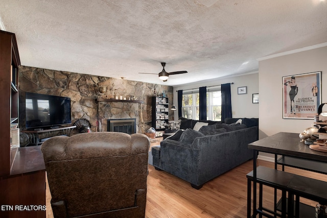 living room with a stone fireplace, light wood-type flooring, a textured ceiling, and crown molding