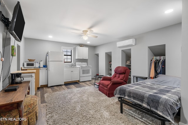 bedroom featuring an AC wall unit, sink, white refrigerator, light hardwood / wood-style floors, and ceiling fan