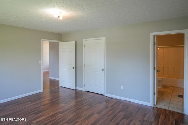 unfurnished bedroom with a closet, a textured ceiling, ensuite bathroom, and dark hardwood / wood-style flooring