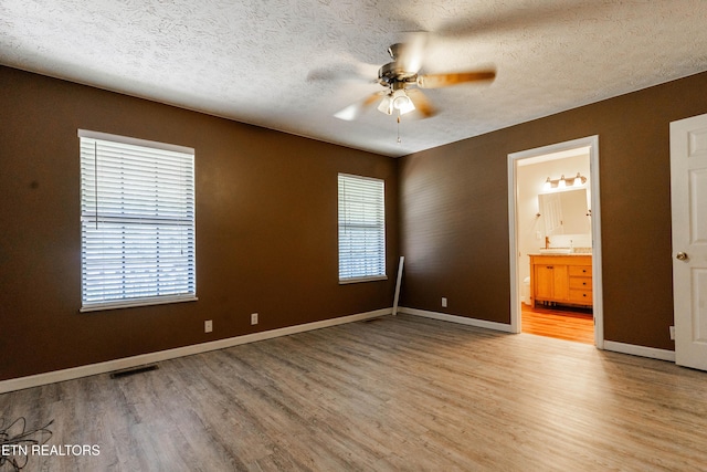 unfurnished bedroom featuring ensuite bath, ceiling fan, a textured ceiling, and hardwood / wood-style flooring