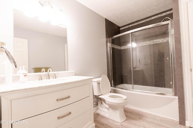 full bathroom featuring vanity, a textured ceiling, enclosed tub / shower combo, hardwood / wood-style floors, and toilet