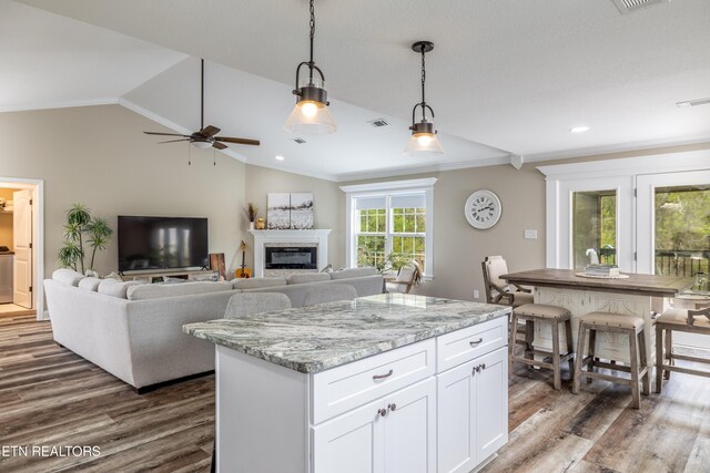 kitchen with light stone countertops, dark hardwood / wood-style flooring, lofted ceiling, decorative light fixtures, and white cabinets