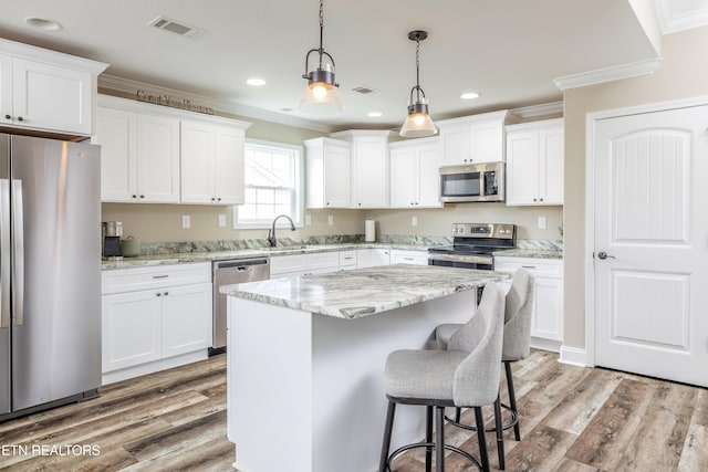 kitchen featuring pendant lighting, a center island, white cabinets, light wood-type flooring, and stainless steel appliances