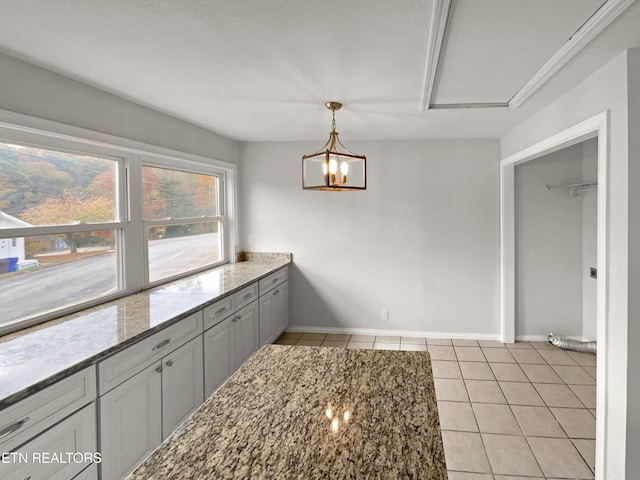 kitchen with dark stone counters, a notable chandelier, gray cabinetry, light tile patterned flooring, and decorative light fixtures