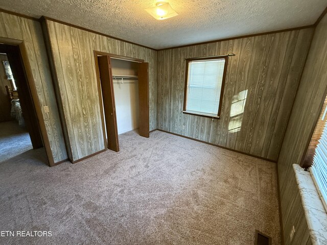 unfurnished bedroom with a textured ceiling, multiple windows, light colored carpet, and a closet