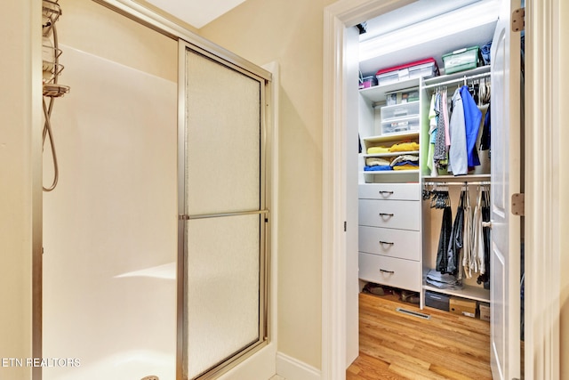 bathroom featuring a stall shower, a walk in closet, and wood finished floors