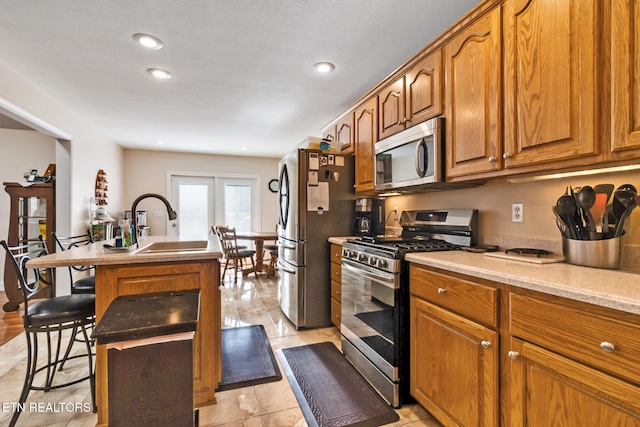 kitchen featuring brown cabinetry, an island with sink, appliances with stainless steel finishes, light countertops, and a sink