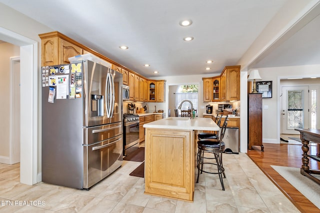 kitchen featuring a center island with sink, glass insert cabinets, stainless steel appliances, light countertops, and a sink