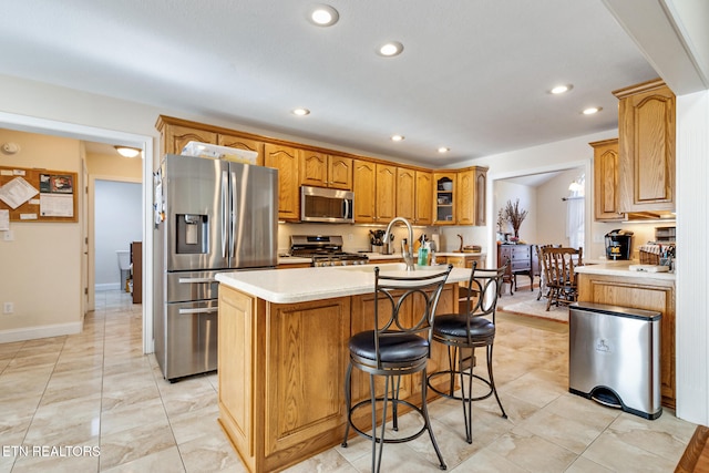 kitchen with an island with sink, glass insert cabinets, brown cabinets, stainless steel appliances, and light countertops