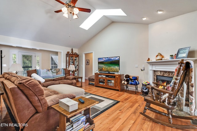 living area featuring high vaulted ceiling, a premium fireplace, a skylight, wood finished floors, and a ceiling fan