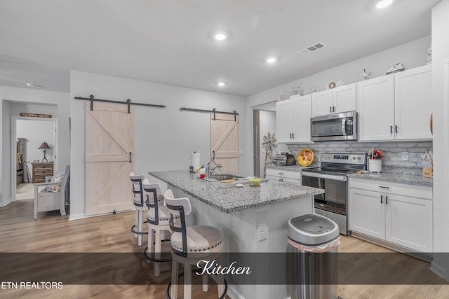 kitchen with light hardwood / wood-style floors, appliances with stainless steel finishes, white cabinetry, and a barn door