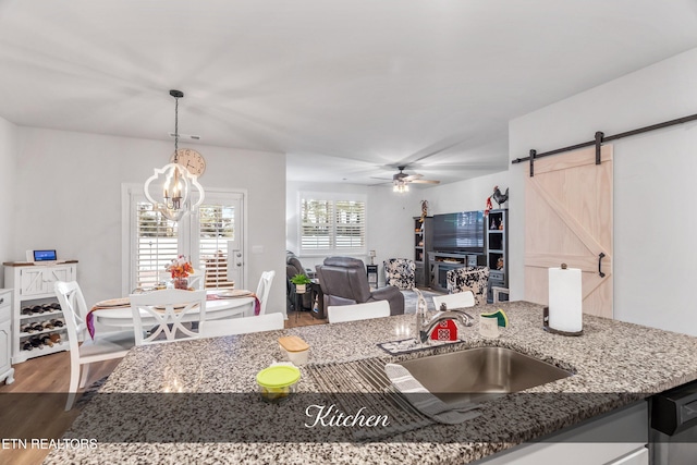 kitchen featuring hardwood / wood-style flooring, dark stone countertops, ceiling fan with notable chandelier, pendant lighting, and sink