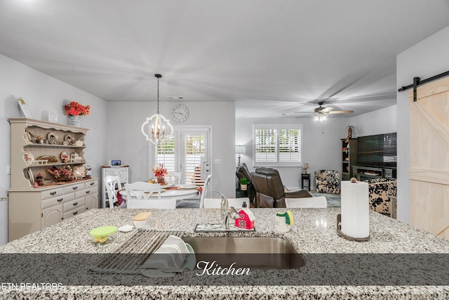 kitchen featuring a barn door, hanging light fixtures, ceiling fan with notable chandelier, and an island with sink