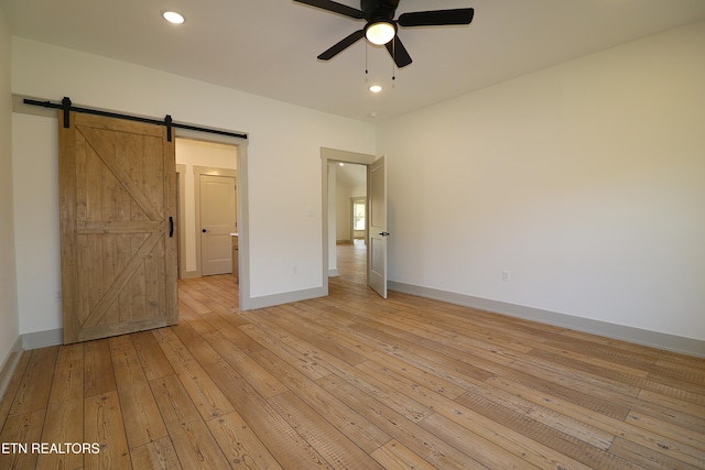 unfurnished bedroom featuring a barn door, light wood-type flooring, and ceiling fan