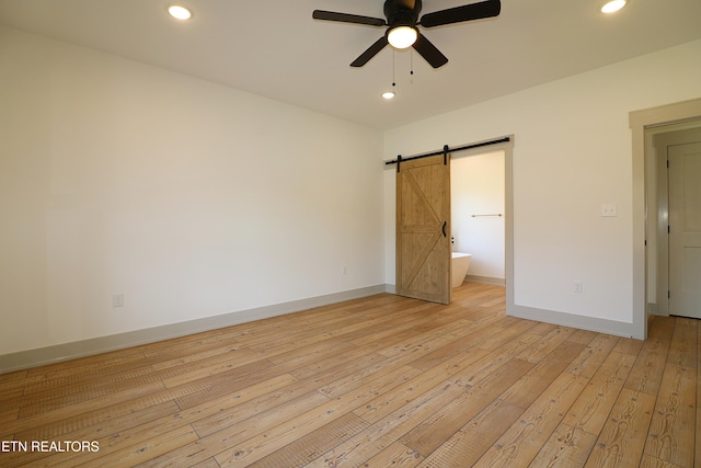 unfurnished bedroom with light hardwood / wood-style floors, ensuite bathroom, a barn door, and ceiling fan