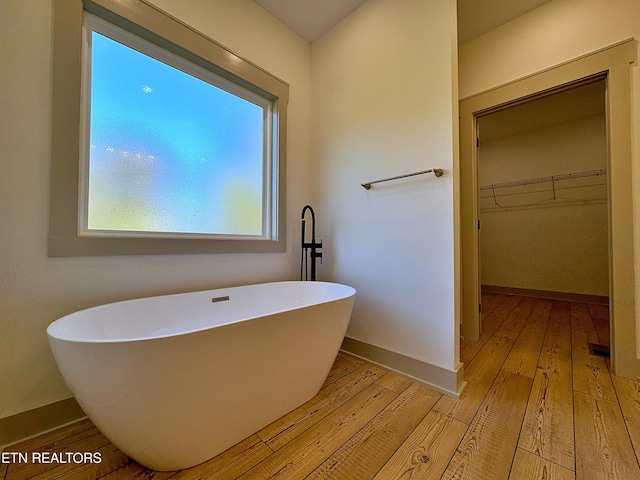 bathroom featuring wood-type flooring, baseboards, a walk in closet, and a freestanding bath