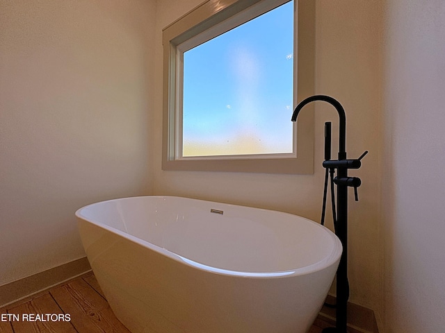 bathroom with baseboards, a freestanding tub, and wood finished floors