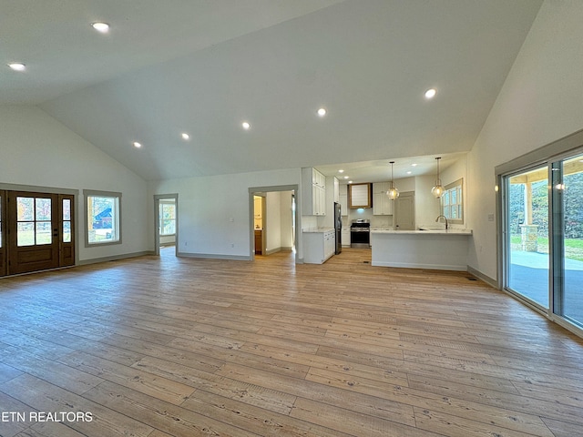 unfurnished living room with high vaulted ceiling, baseboards, light wood-type flooring, and a wealth of natural light