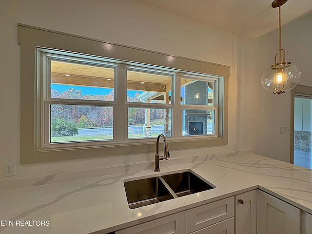 kitchen featuring a sink, white cabinets, light stone countertops, and pendant lighting