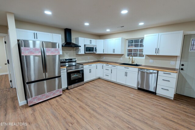 kitchen featuring appliances with stainless steel finishes, wall chimney exhaust hood, sink, white cabinetry, and butcher block counters