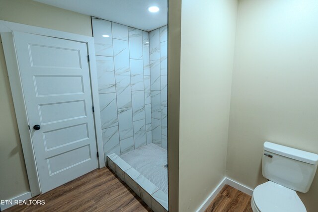 bathroom featuring wood-type flooring, a tile shower, and toilet