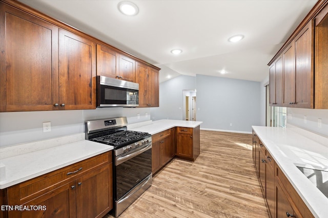 kitchen with light stone counters, light wood-type flooring, vaulted ceiling, and appliances with stainless steel finishes