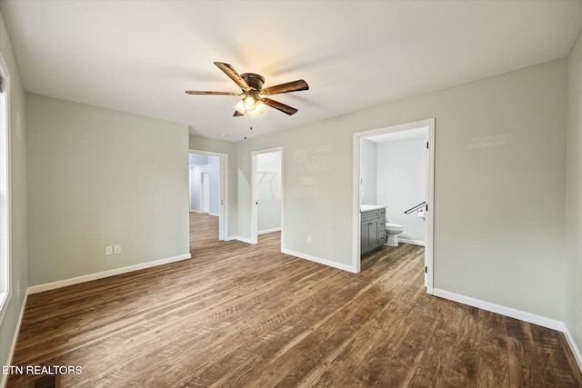 unfurnished bedroom with ensuite bath, ceiling fan, dark wood-type flooring, a walk in closet, and a closet