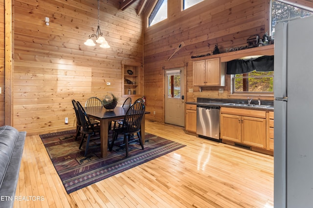 dining room with wood walls, sink, light wood-type flooring, and high vaulted ceiling