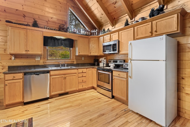 kitchen with lofted ceiling with beams, appliances with stainless steel finishes, wood walls, sink, and light hardwood / wood-style flooring