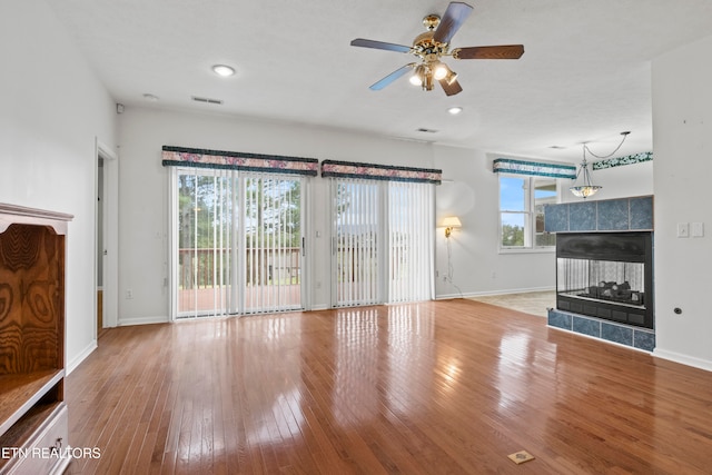 unfurnished living room featuring light wood-type flooring, a tiled fireplace, a healthy amount of sunlight, and ceiling fan