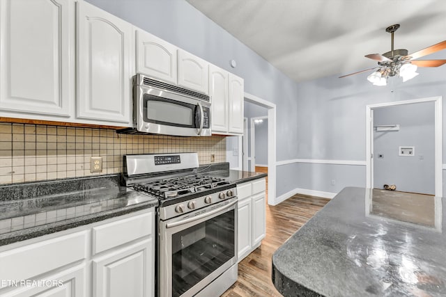 kitchen with tasteful backsplash, appliances with stainless steel finishes, light wood-type flooring, white cabinetry, and dark stone countertops