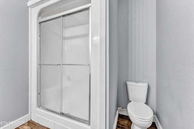 bathroom with toilet, a shower with shower door, and hardwood / wood-style floors