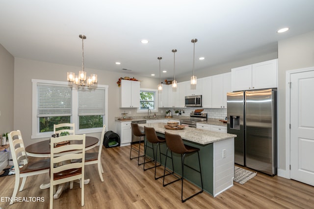 kitchen featuring a kitchen island, light hardwood / wood-style flooring, white cabinets, decorative light fixtures, and appliances with stainless steel finishes