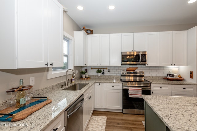 kitchen with sink, stainless steel appliances, white cabinets, light stone counters, and light hardwood / wood-style flooring