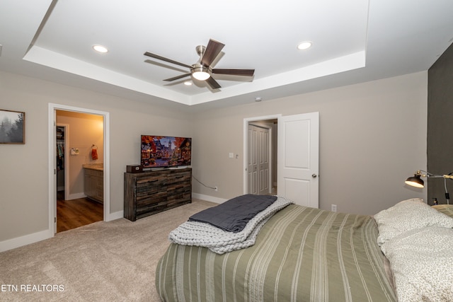 bedroom with ensuite bath, ceiling fan, light colored carpet, and a raised ceiling