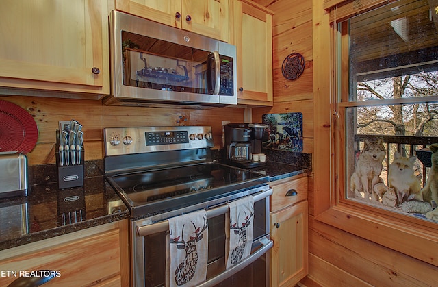 kitchen with wood walls, light brown cabinets, dark stone counters, and appliances with stainless steel finishes