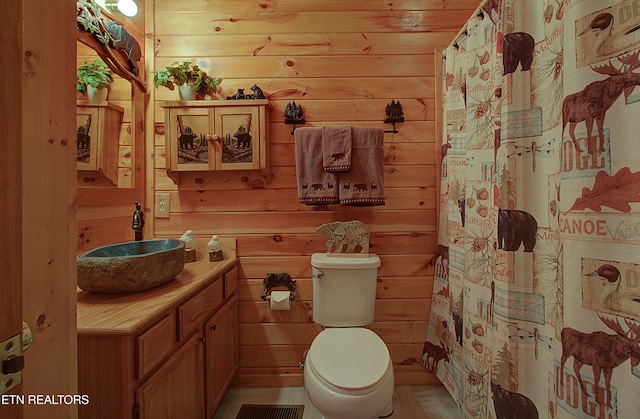 bathroom featuring curtained shower, wooden walls, vanity, and toilet