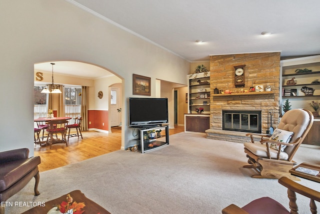 living room featuring an inviting chandelier, built in features, light hardwood / wood-style floors, a fireplace, and ornamental molding