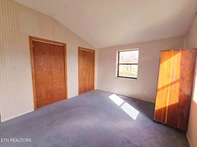 unfurnished bedroom with multiple closets, vaulted ceiling, and dark carpet