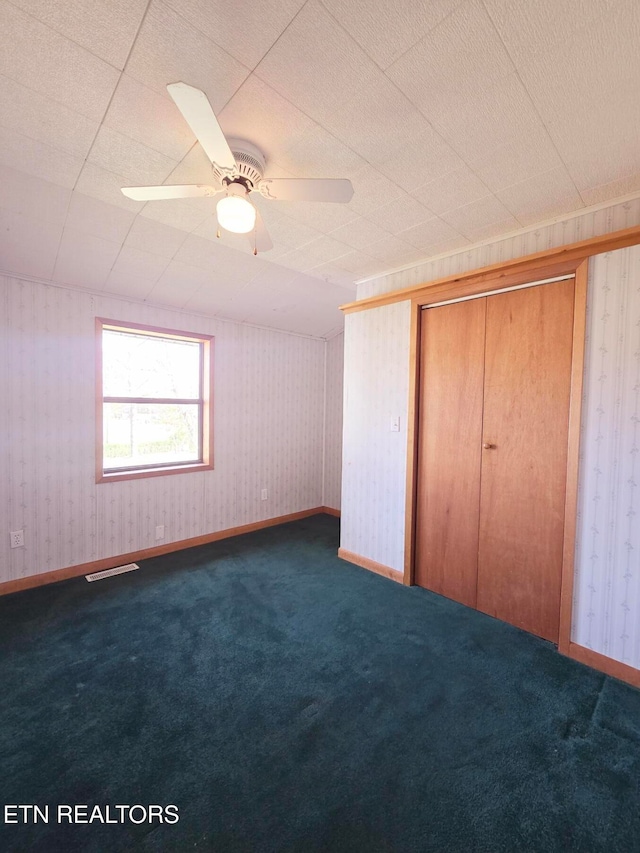 unfurnished bedroom with a closet, dark carpet, and ceiling fan