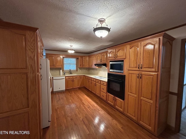 kitchen with white appliances, tasteful backsplash, sink, light wood-type flooring, and a textured ceiling