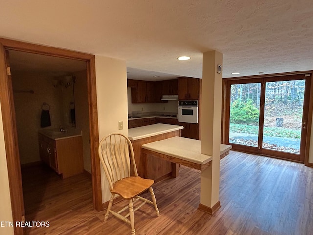 kitchen with oven, wood-type flooring, a textured ceiling, kitchen peninsula, and stovetop