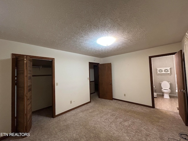 unfurnished bedroom featuring ensuite bathroom, a textured ceiling, a closet, and light colored carpet